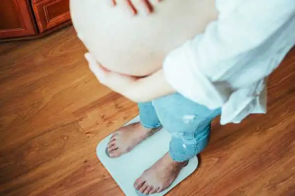 Image of woman weighing herself and experiencing weight gain through pregnancy Shettleston